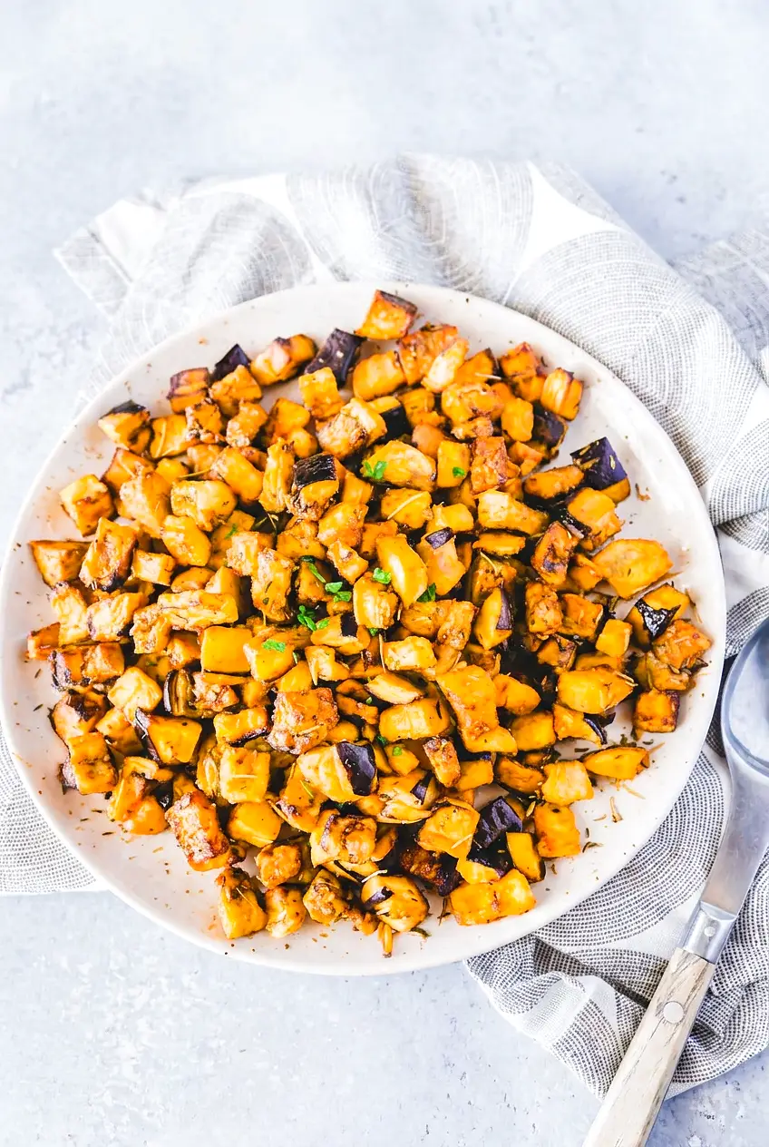 Crispy air fryer eggplant cubes with browned edges, sprinkled with chopped parsley in a shallow ceramic bowl.