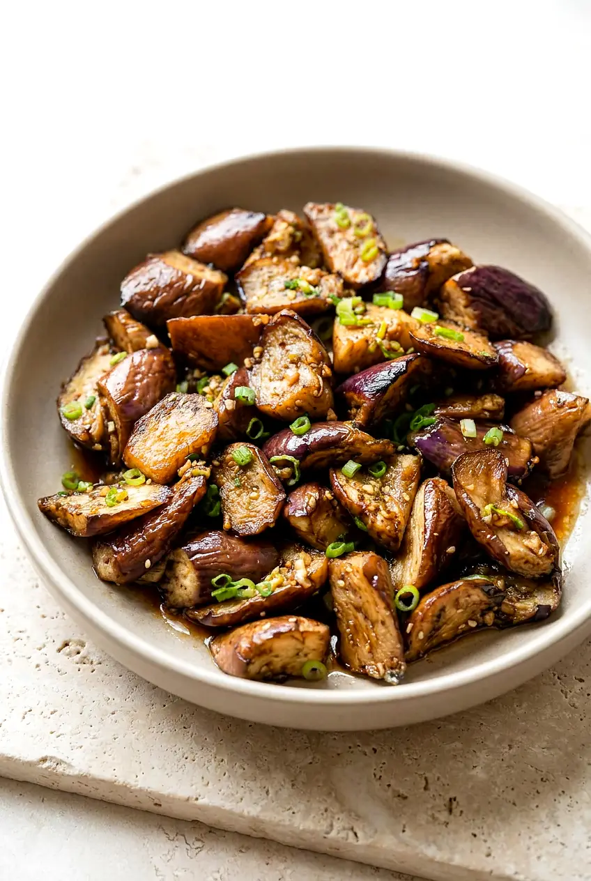 Air fryer Chinese eggplant in glossy garlic-soy-black vinegar glaze, browned edges, wrinkled skins, sliced scallion garnish.