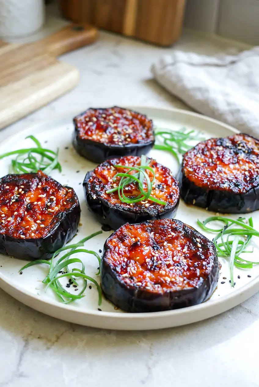 Air Fryer Miso Glazed Eggplant rounds on a plate, glossy caramelized glaze with sesame seeds and sliced green onions.