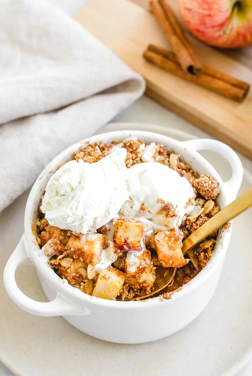 Air fryer apple crisp in a white ramekin topped with vanilla ice cream