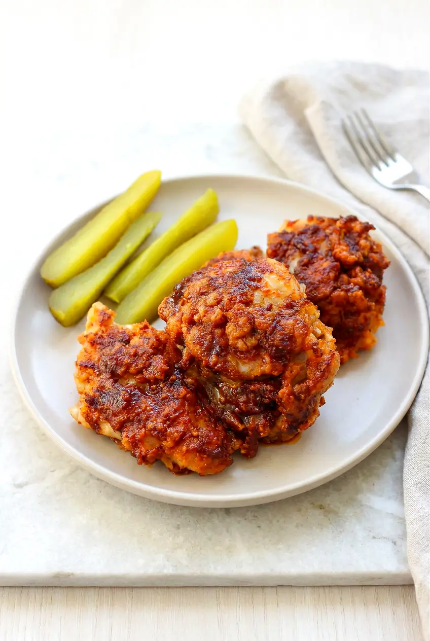 Air Fryer Nashville hot chicken thighs plated with dill pickle chips and spicy butter glaze