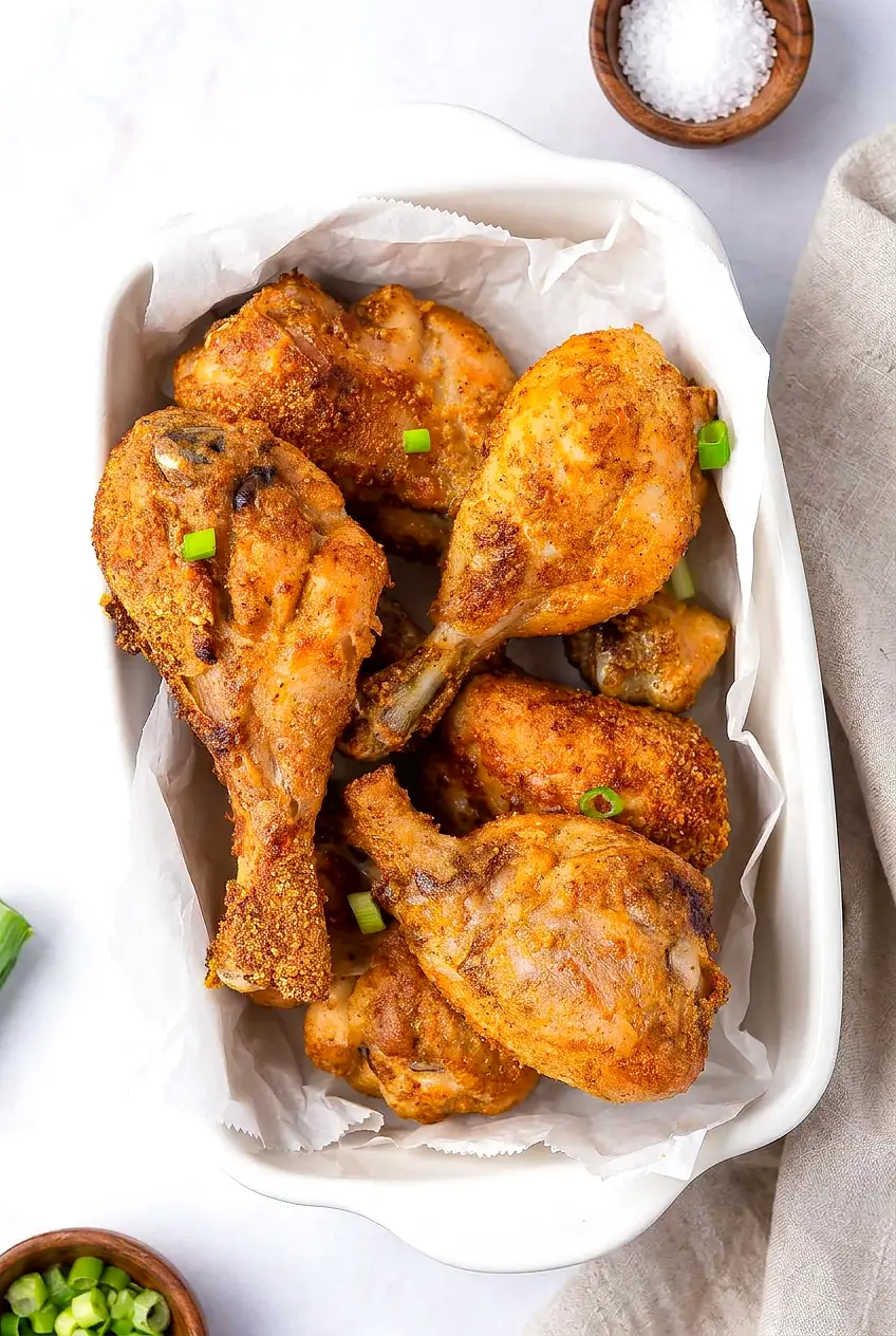 Air Fryer Garlic Parmesan Chicken Legs served in a parchment-lined baking dish with golden browned skin