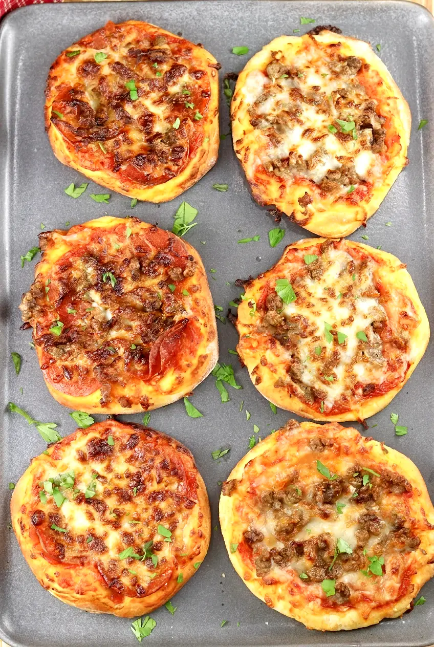 Air fryer mini pizzas on a gray platter, topped with pepperoni, sausage, and melted cheese, overhead view
