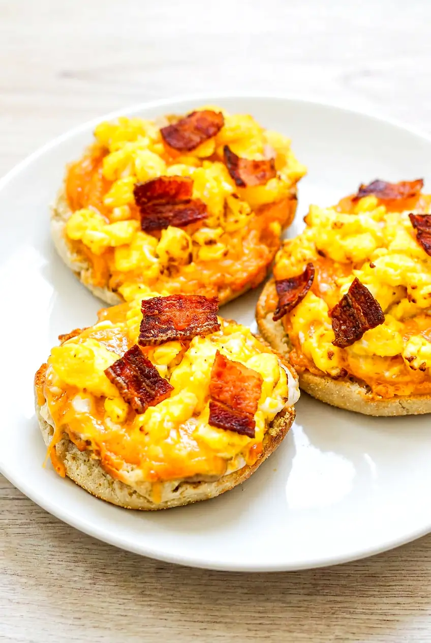 Air fryer English muffin breakfast pizza served on a plate with melted cheddar, eggs, bacon, and crisp muffin edges.