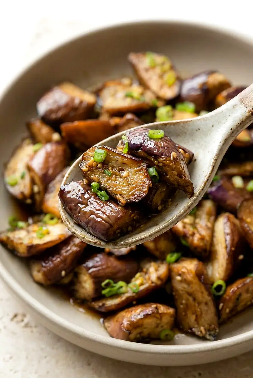 Close-up of air fryer Chinese eggplant showing tender interior, blistered skin, and glossy soy-garlic glaze with sliced scallions.
