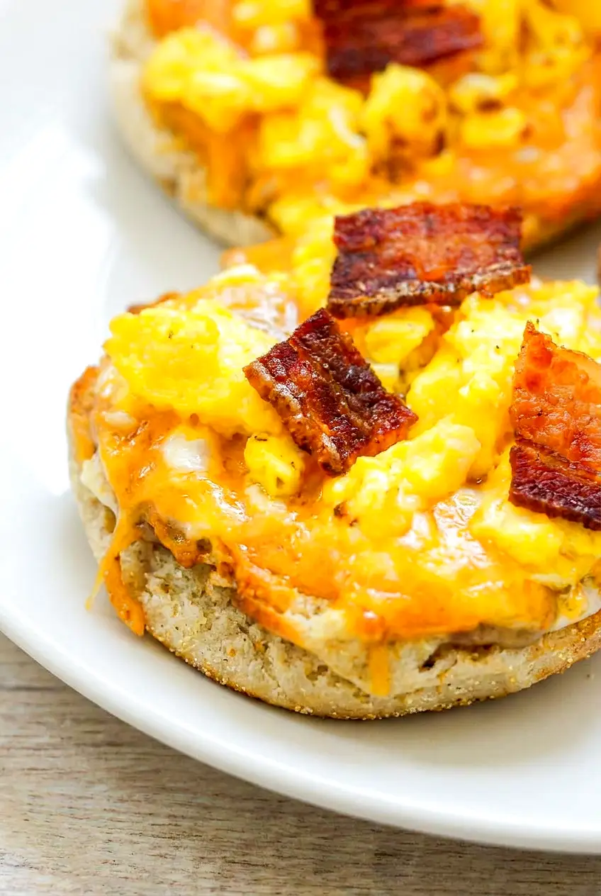 Close-up of air fryer English muffin breakfast pizza showing melted cheese, chopped bacon, and a crisp toasted muffin base.