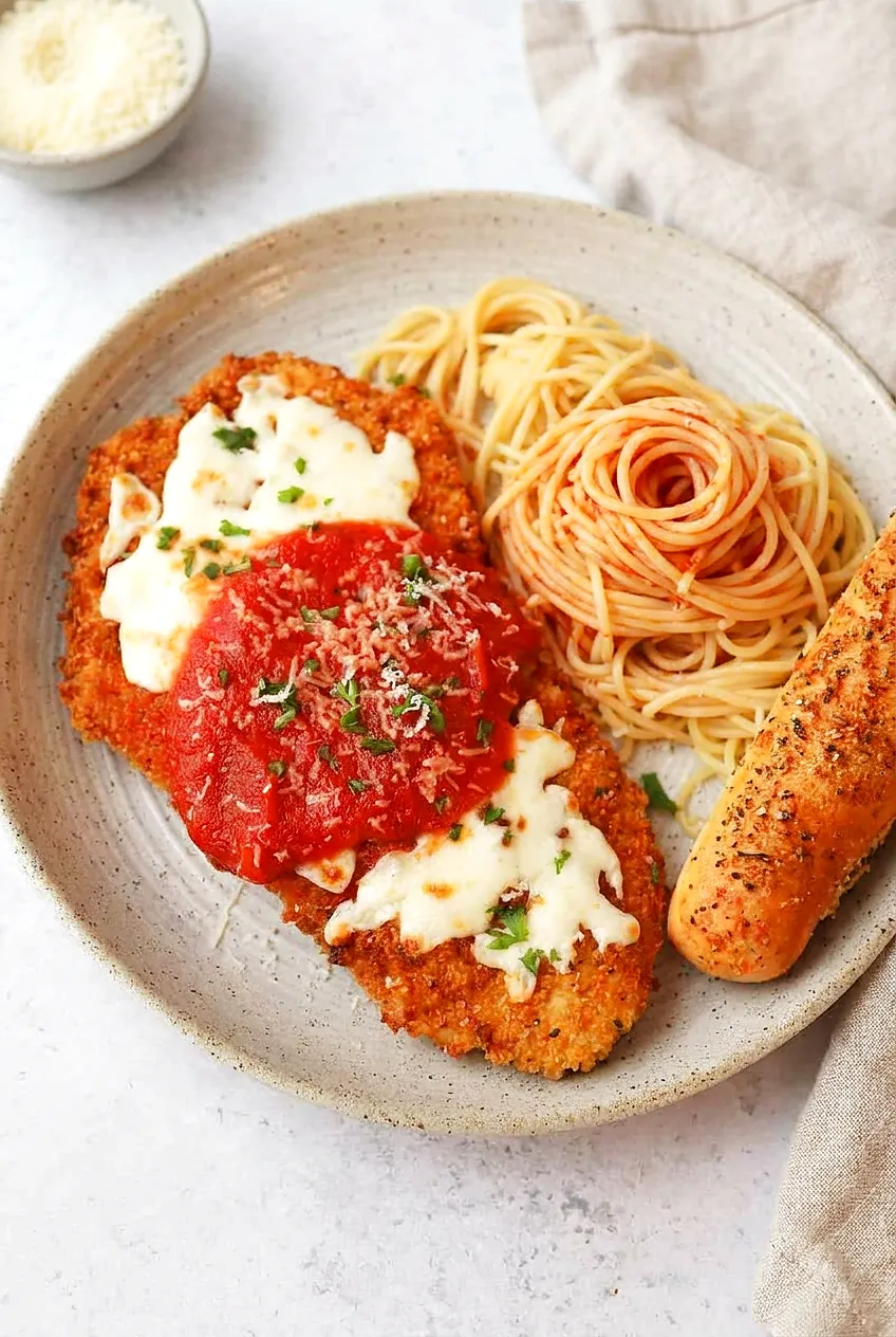 Air Fryer Chicken Breast Parmesan on a speckled platter with melted mozzarella and marinara, plus spaghetti and a breadstick.