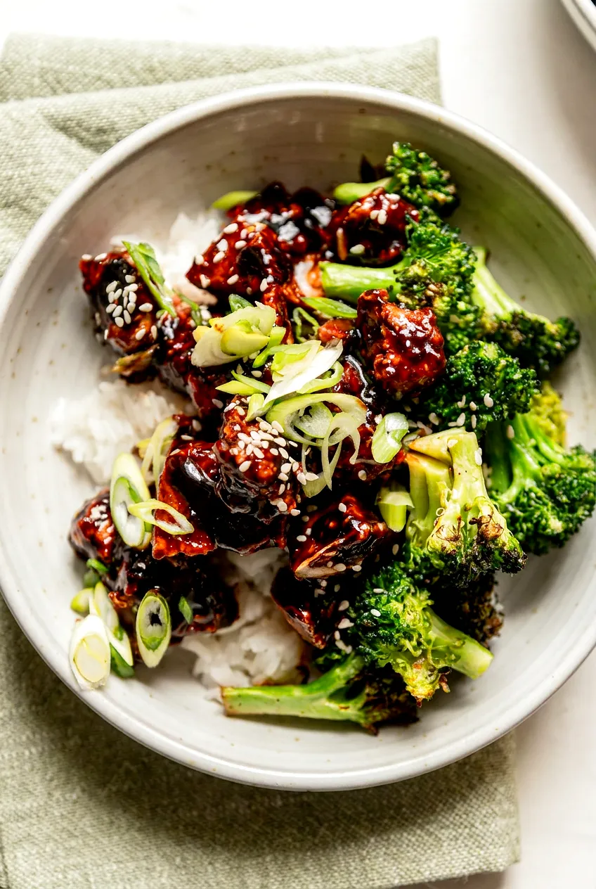 Overhead bowl of rice with Air Fryer Teriyaki Tofu and broccoli, glossy glaze, crisp edges, sesame seeds and sliced green onions.