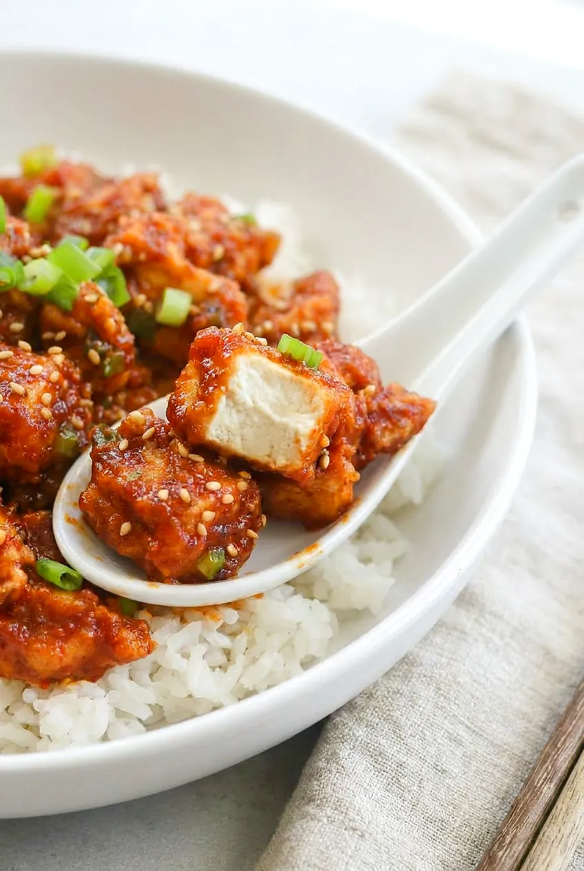 Close-up of Air Fryer Gochujang Tofu showing crisp edges under a sticky glaze, with sesame seeds and green onion slices.