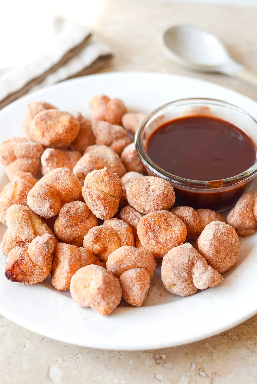 Air Fryer Churro Bites on a white plate, cinnamon-sugar coated, with a small bowl of chocolate dip; golden and lightly crisp.