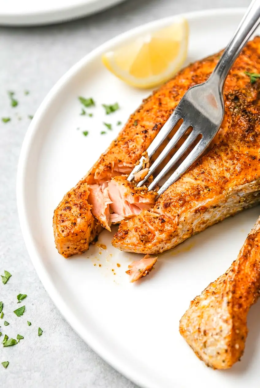 Close-up air fryer salmon steak flaked open, juicy flaky center with browned, seasoned edges and a lemon wedge
