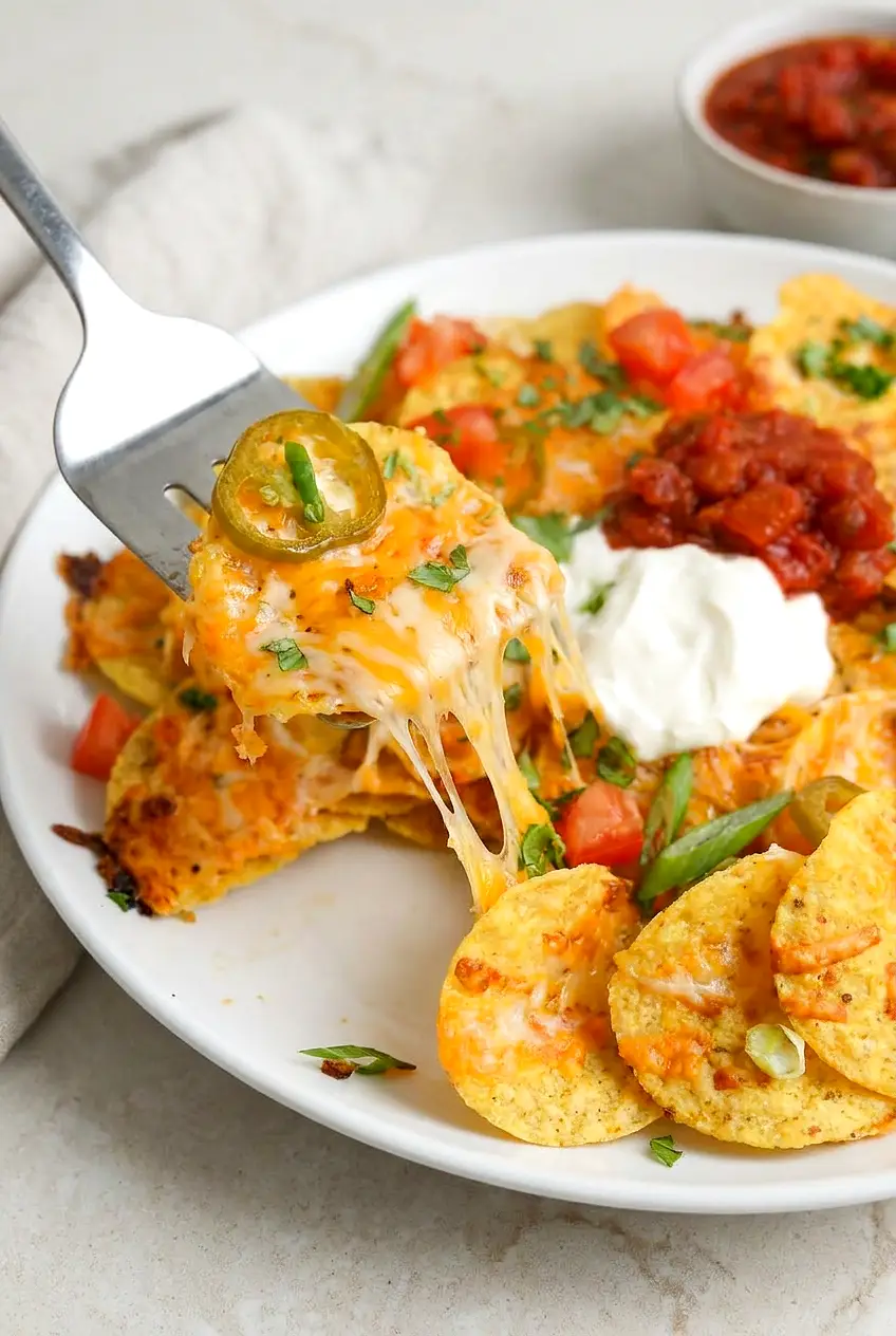 Close-up of Air Fryer Loaded Nachos with a cheese pull, crisp chip edges, jalapeño slices, and a touch of salsa and sour cream on top.