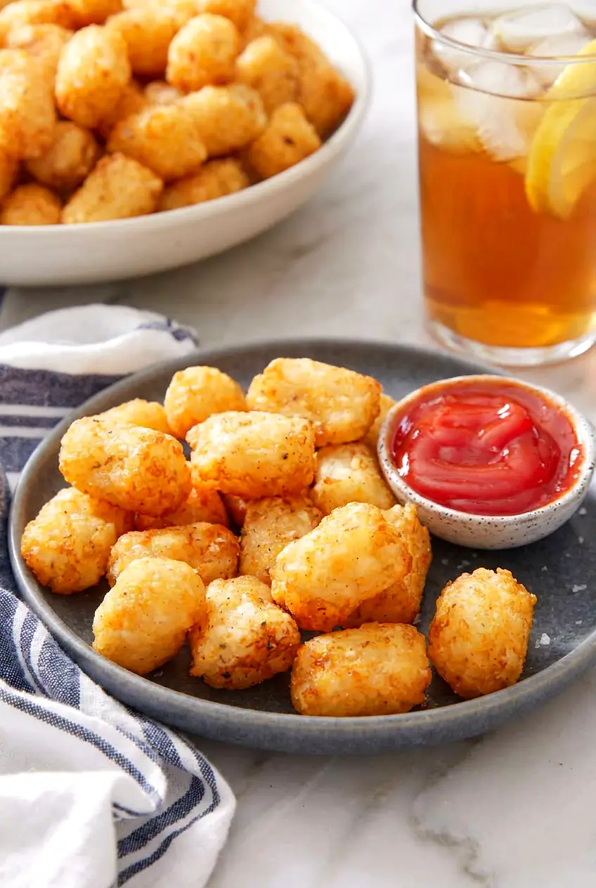 Air fryer tater tots on a plate with a bowl of ketchup and a drink in the background.