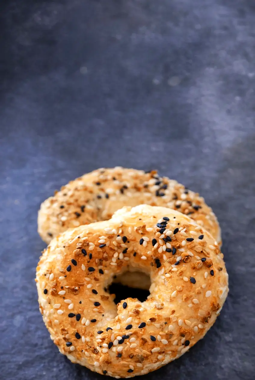 Two ingredient bagels on a dark surface with light browning and Everything Bagel seasoning