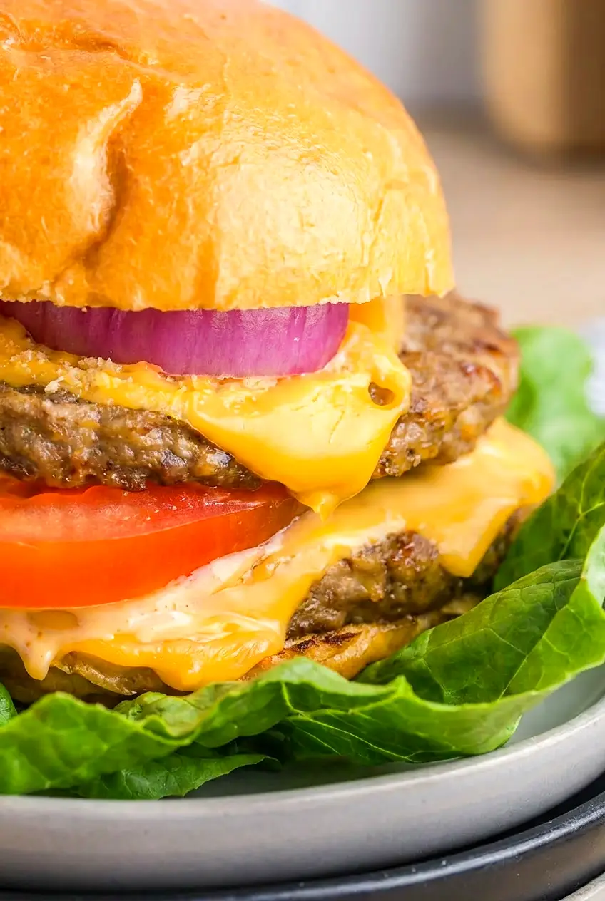 Close-up of an air fryer frozen hamburger with browned edges and melted cheese on a bun.