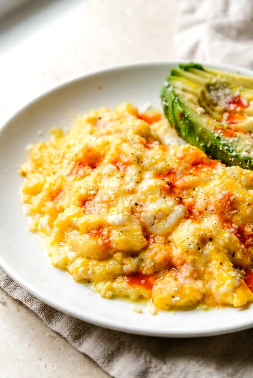 Close-up of creamy air fryer scrambled eggs with soft curds, avocado, and hot sauce