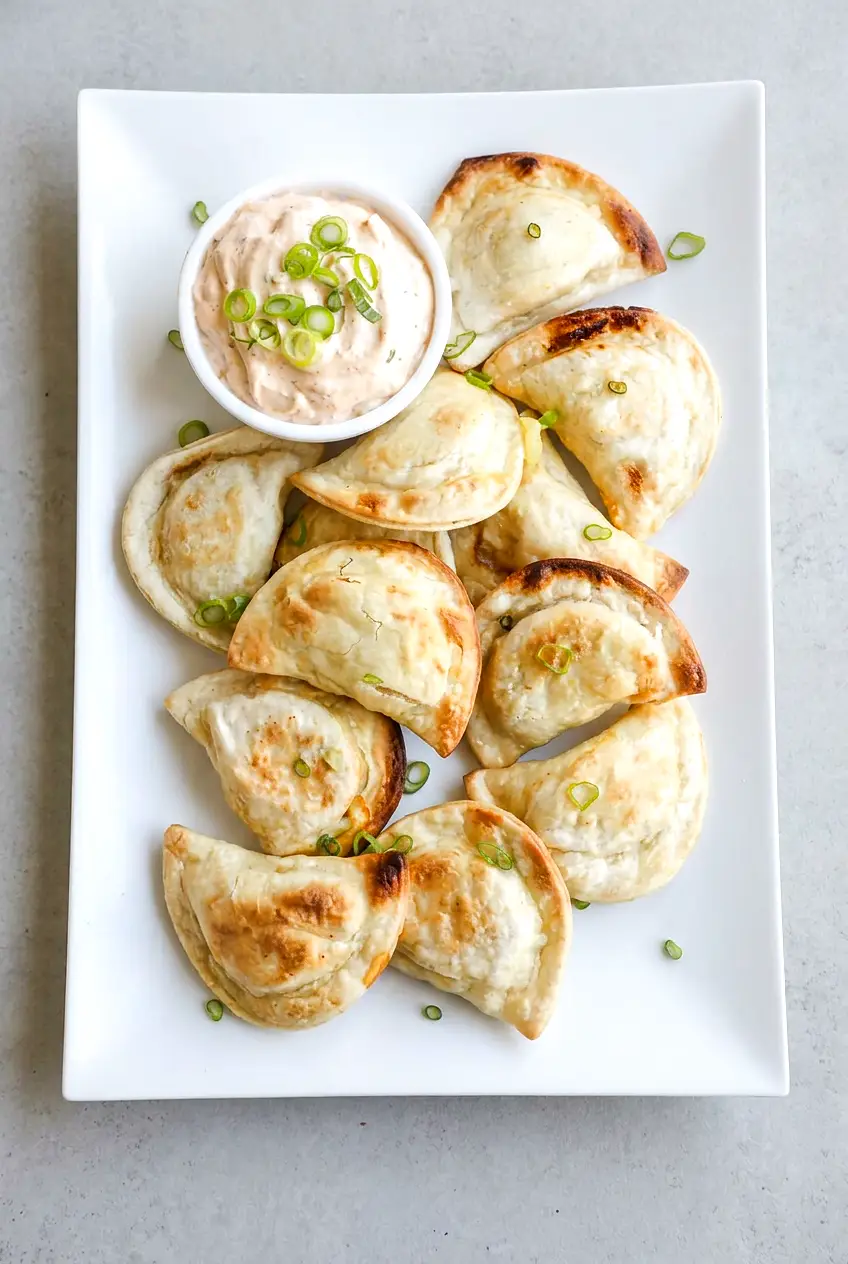 Air fryer pierogies on a white platter with sour cream and sliced green onions