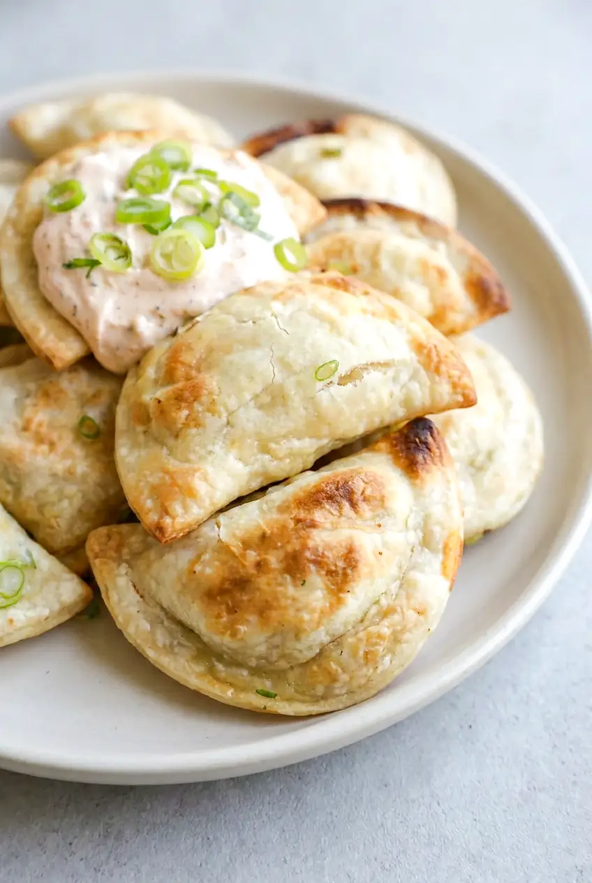 Close-up of air fryer pierogies with crisp browned spots, sour cream, and green onion garnish