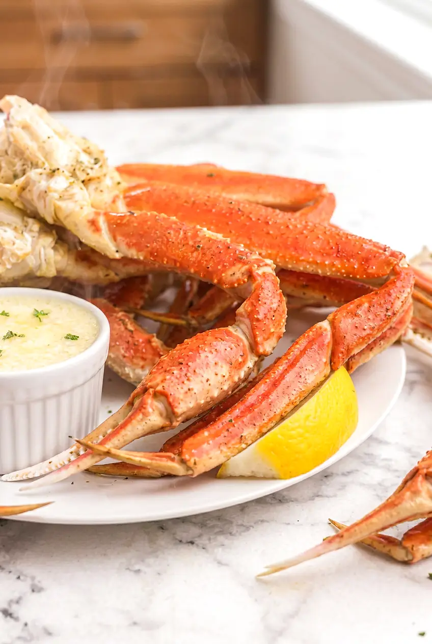 Close-up of air fryer crab legs with moist orange shells, lemon wedges, and melted butter