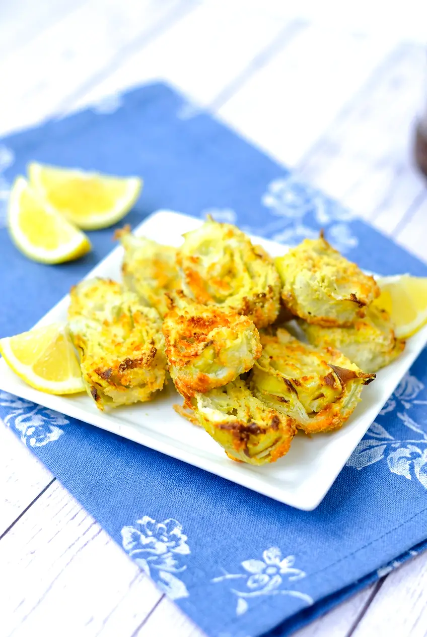 Air fryer artichoke hearts on a white plate with lemon, served over a blue floral napkin on a white table