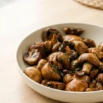 Air fryer garlic mushrooms browned in spots and tossed with garlic butter and chopped parsley in a shallow bowl.