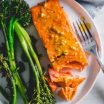 Garlic-seasoned air fryer salmon fillet with broccolini on a white plate.