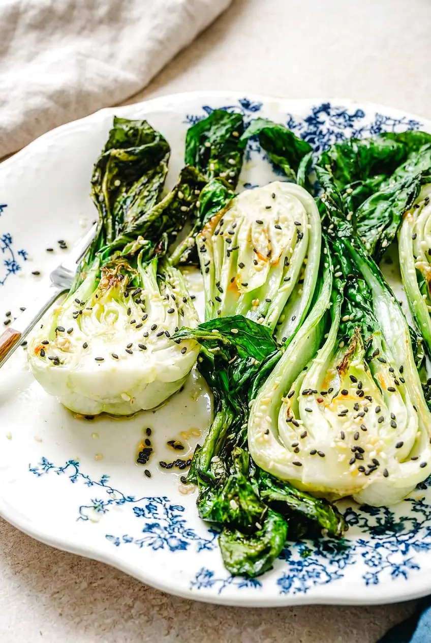 Close-up of air fryer bok choy showing crisp-tender stems, wilted leaves, and browned edges on a blue plate